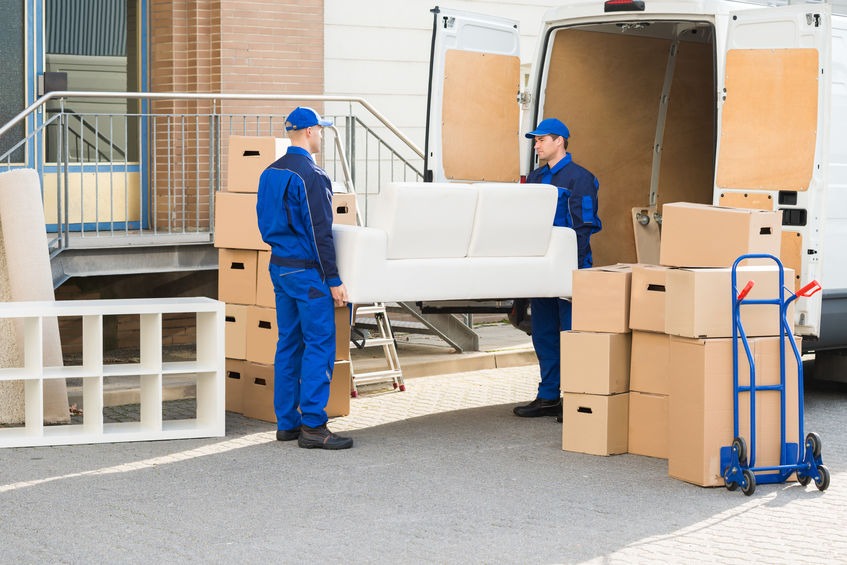 Photo de 2 déménageurs habillés en bleu transportant un canapé droi blanc en tissu